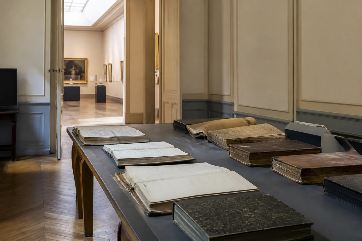 Salle de lecture d&rsquo;archives avec registres reliés sur une longue table